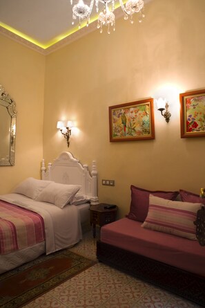 A bedroom with two beds, a chandelier, wall sconces, and floral artwork.