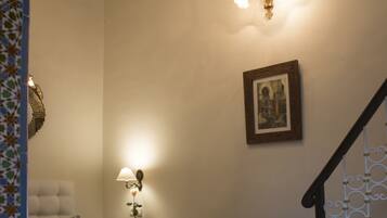 A bedroom with a bed, a nightstand, a wall-mounted lamp, a framed picture, a wicker chair, and a staircase.