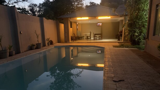 A swimming pool with a tiled deck and a covered patio area with seating. - LePatino Bed & Breakfast (Livingstone)