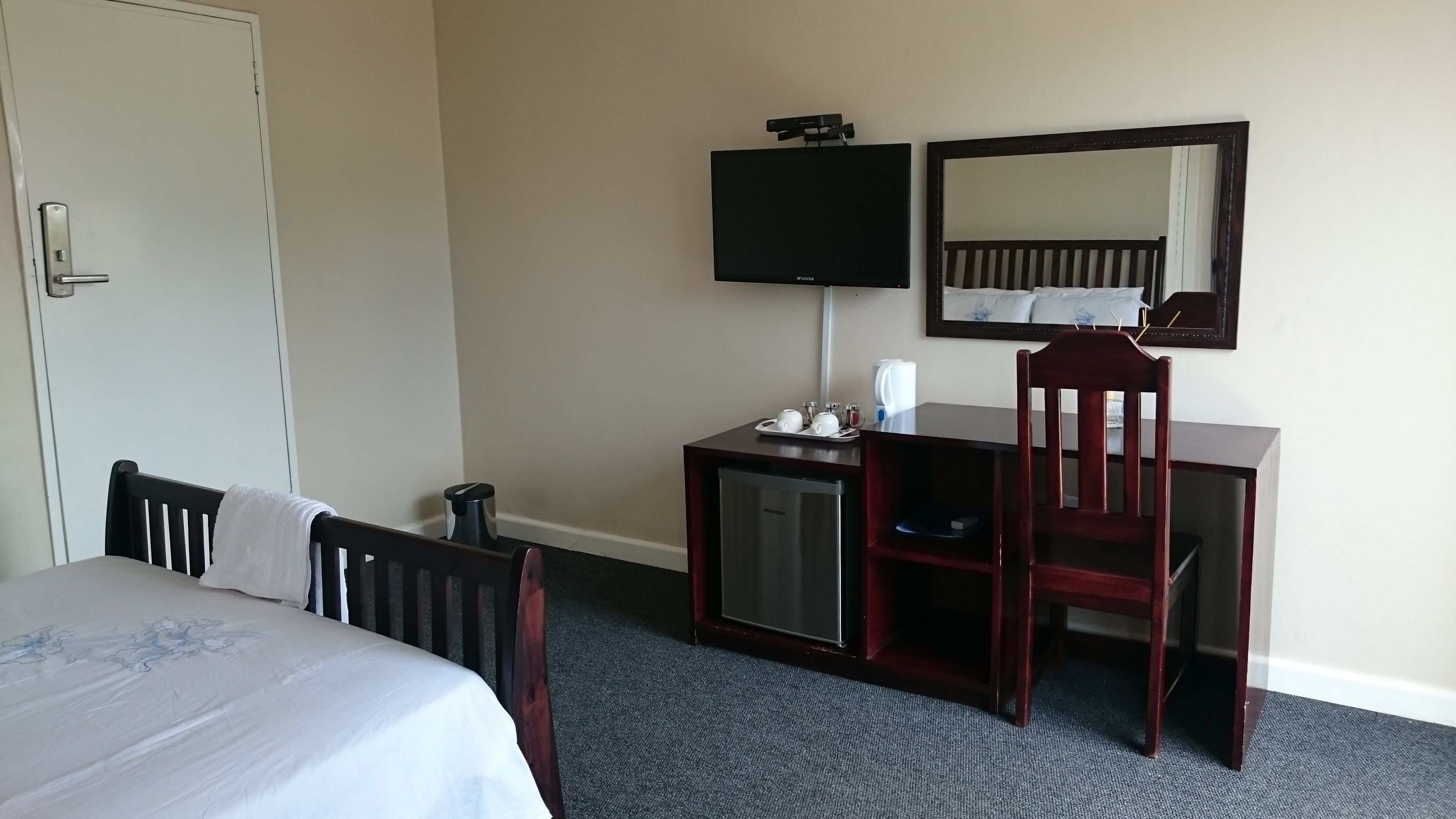 A hotel room with a bed, a desk, a chair, a television, and a mirror.