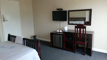 A hotel room with a bed, a desk, a chair, a television, and a mirror.