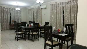 A dining area with a table set for four, surrounded by chairs, with a chandelier above and curtains on the windows. - LePatino Bed & Breakfast (Livingstone)