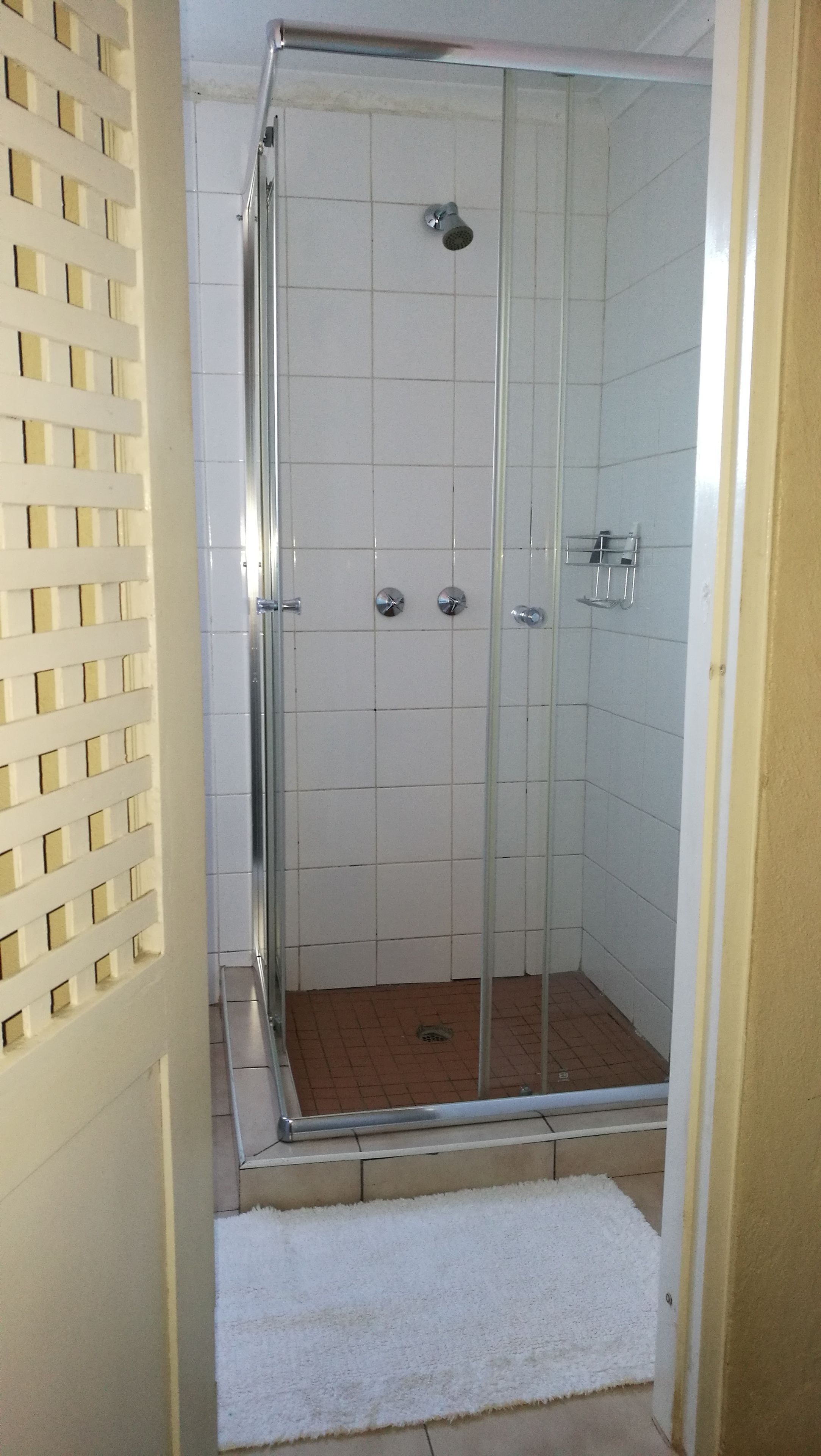 A glass-enclosed shower with a tiled floor and a white mat at the entrance.