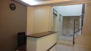 A hallway with a wooden counter, a clock, and a staircase leading to another room. - LePatino Bed & Breakfast (Livingstone)