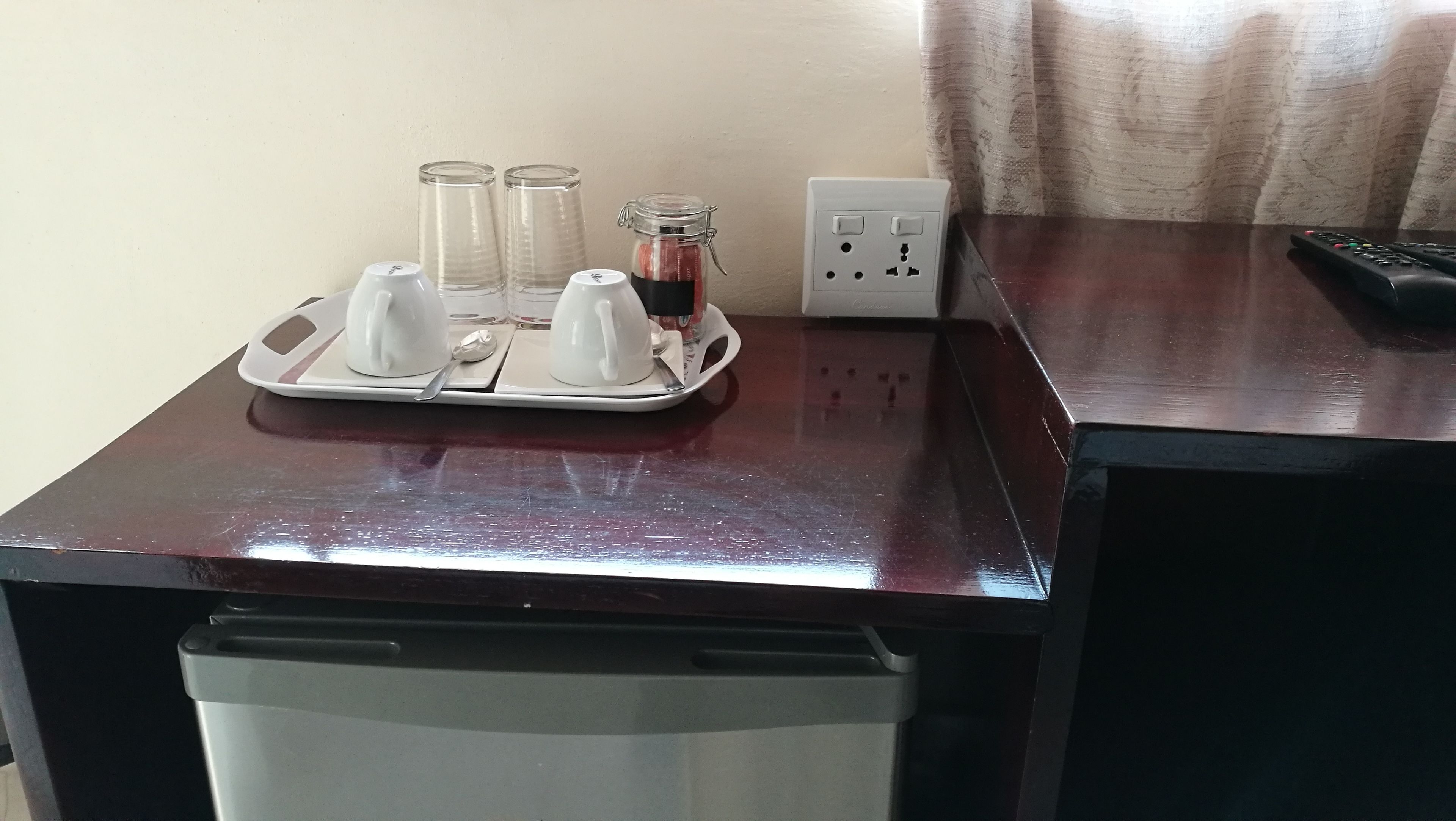 A wooden desk with a tray containing two white cups, a glass jar, and two glasses.