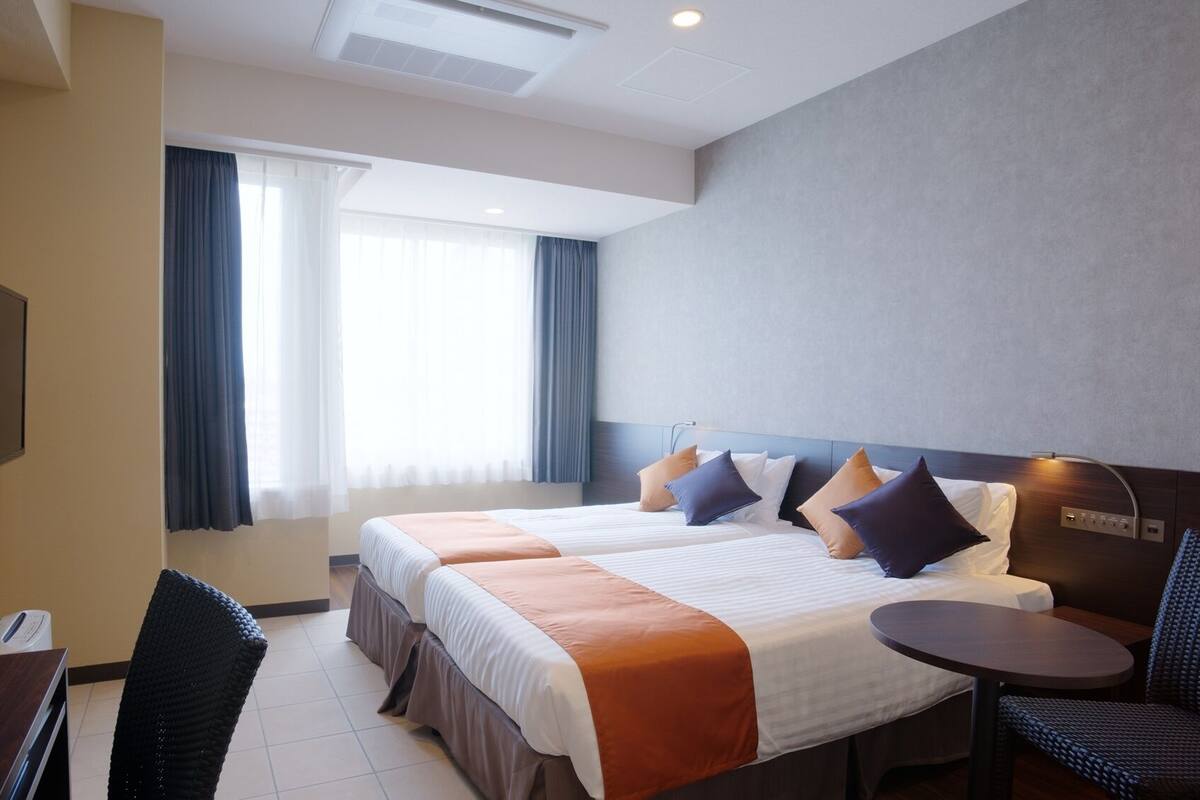 A hotel room with two beds, a TV, a desk, and a chair.