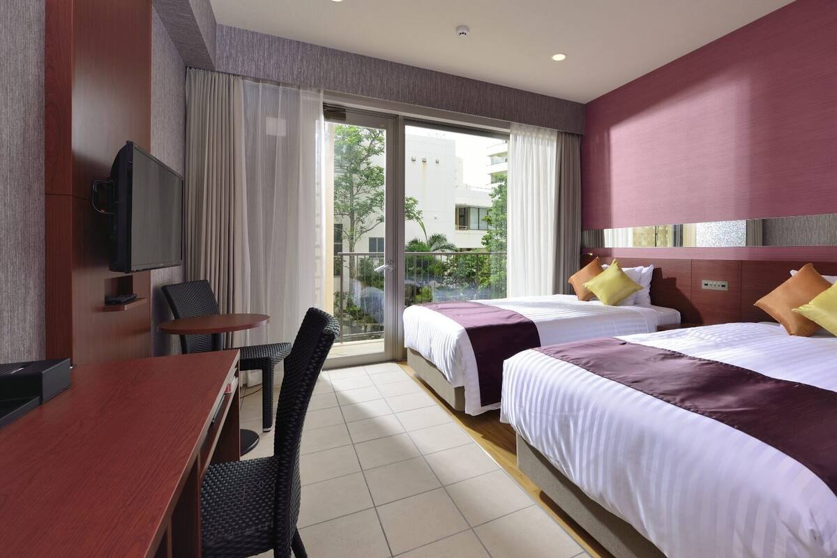 A hotel room with two beds, a TV, a desk, and a chair.