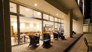 An outdoor seating area with tables and chairs, a covered walkway, and a view into the building. - Community & Spa Naha Central Hotel (Naha)