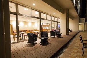 An outdoor seating area with tables and chairs, a covered walkway, and a view into the building.