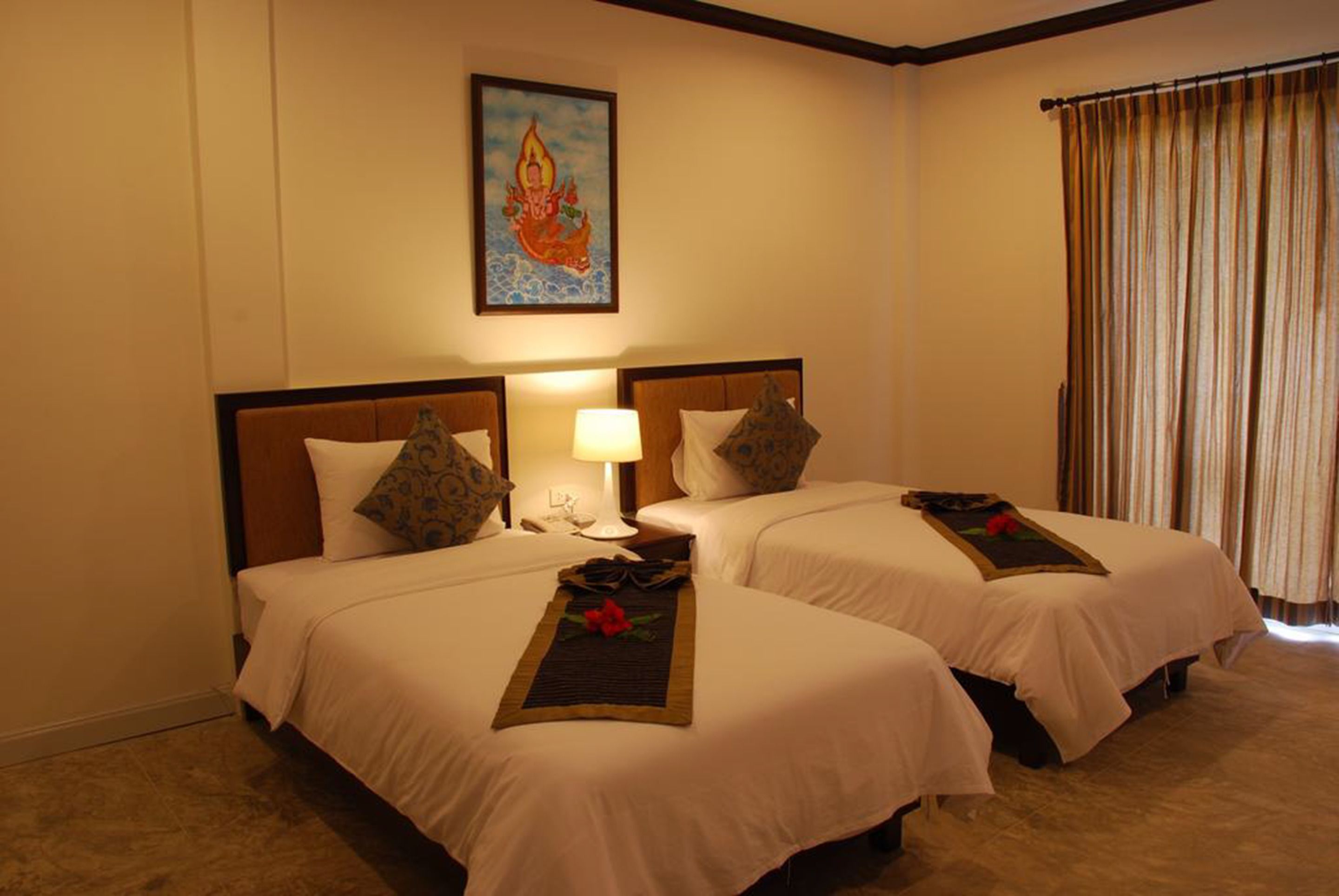 A hotel room with two beds, a nightstand, a lamp, a painting on the wall, and a window with curtains.