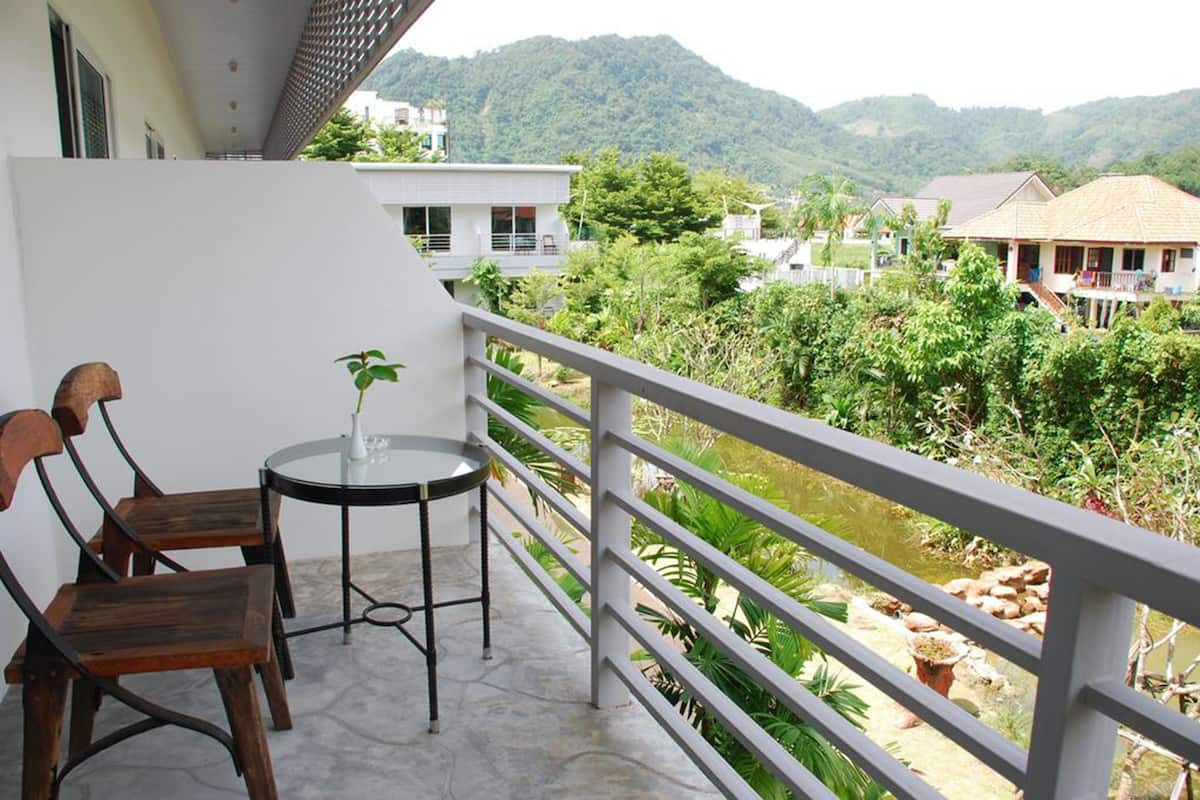 A balcony with two wooden chairs and a small round table, overlooking a lush green landscape with a river and distant buildings.
