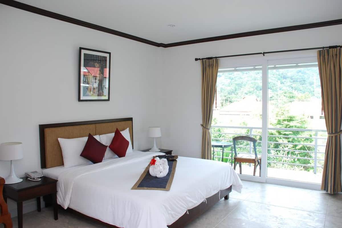 A hotel room with a large bed, a nightstand, a chair by the window, and a view of greenery outside.