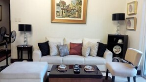 Un salon avec un canapé blanc, une table basse et un fauteuil. Il y a un tableau au mur et une lampe sur une table d’appoint.