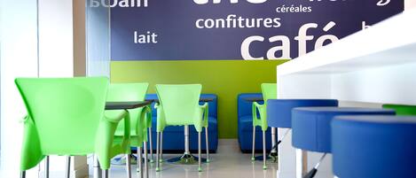 A café interior with green and blue chairs, a word cloud on the wall, and a clean floor.