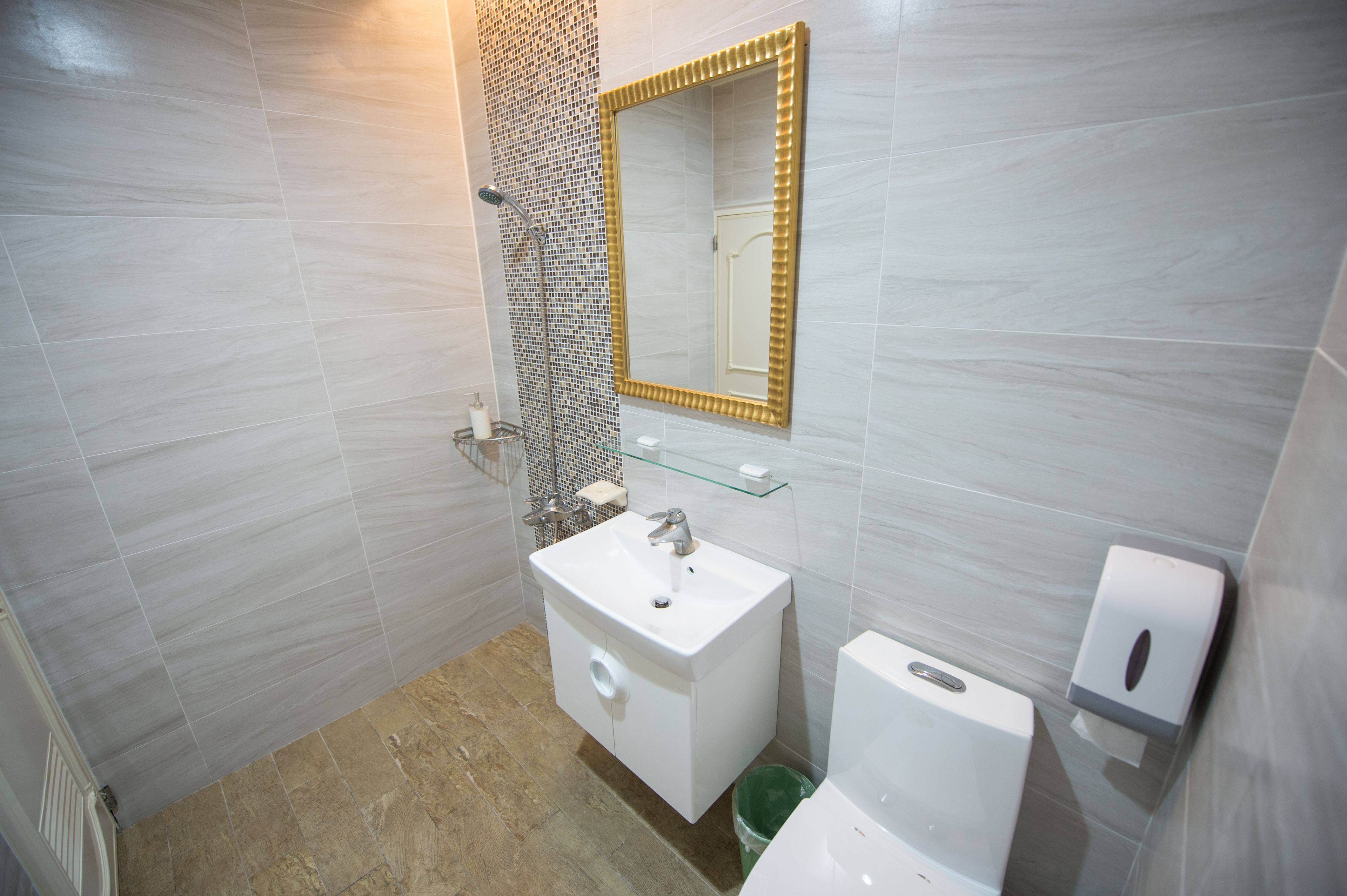 Un bagno con un lavandino bianco, una mensola in vetro, uno specchio con cornice dorata e un water.