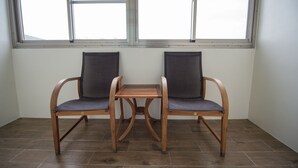 Two wooden chairs with mesh seats and a small wooden table in a room with tiled flooring and large windows.