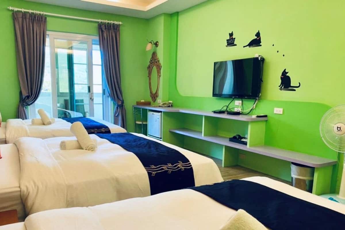 A hotel room with three beds, a TV, a mirror, and a fan.