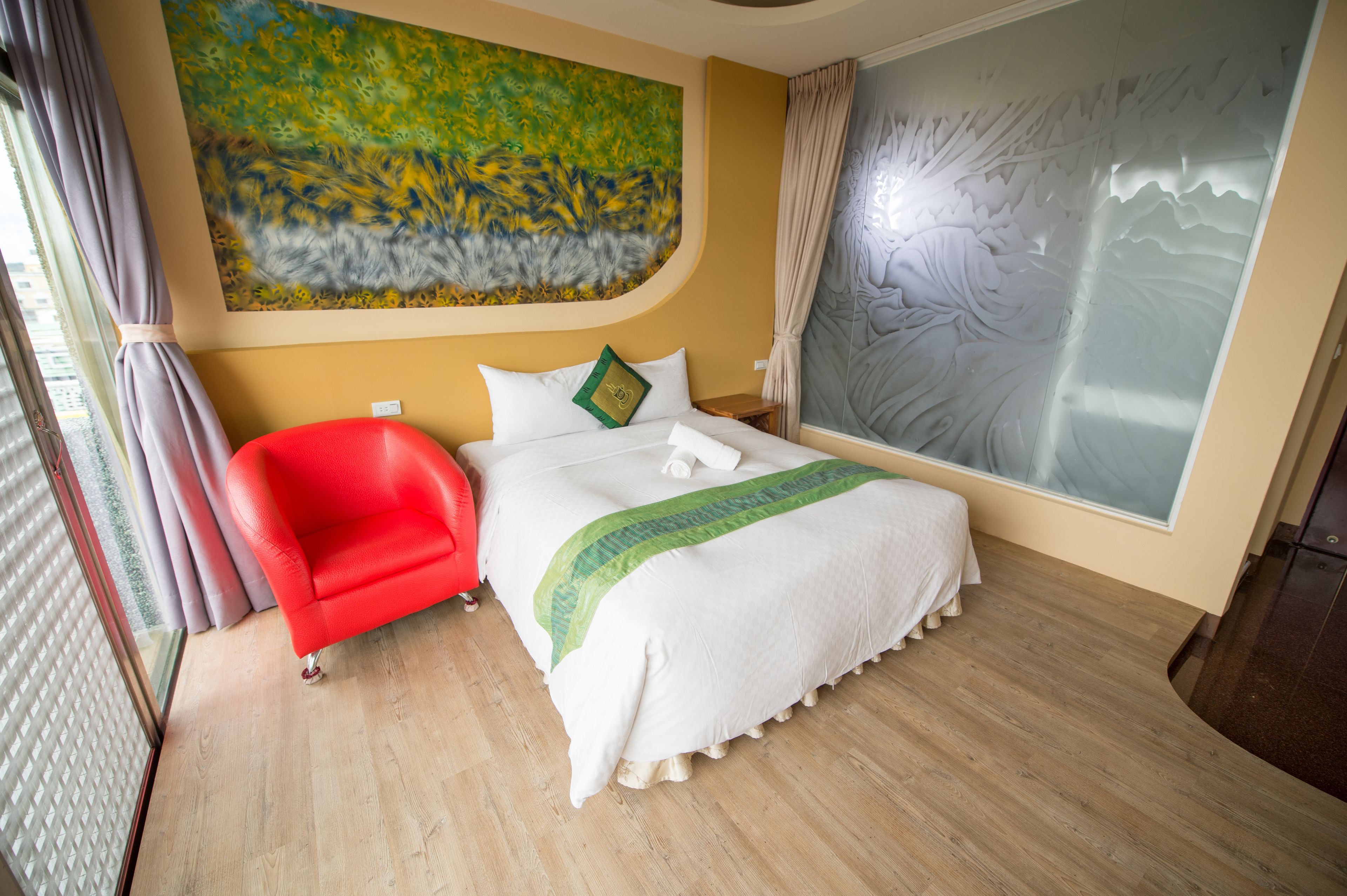 A hotel room with a bed, a red chair, a painting, and a large window with frosted glass.