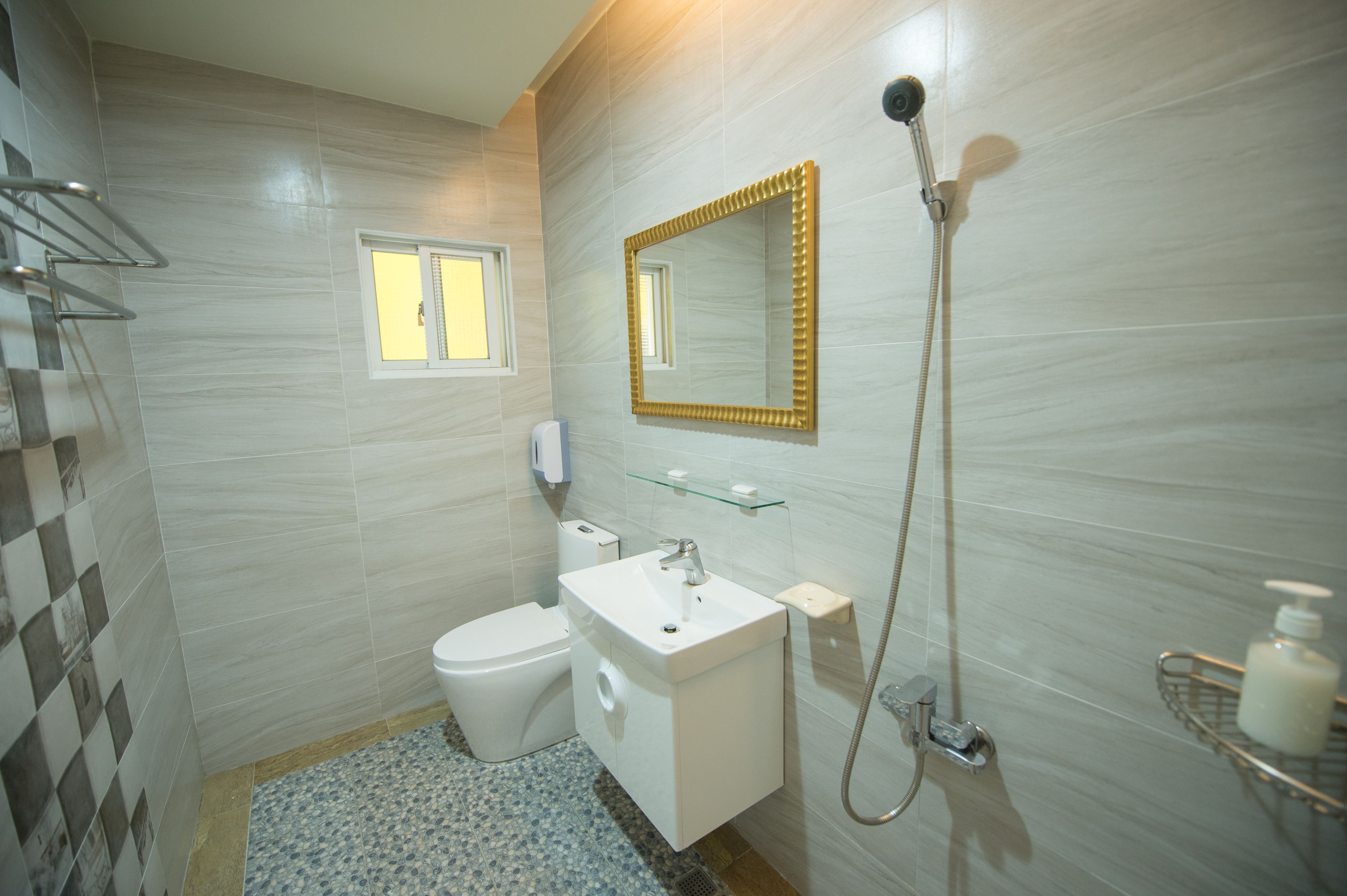 A bathroom with a toilet, sink, mirror, shower, and a small window.