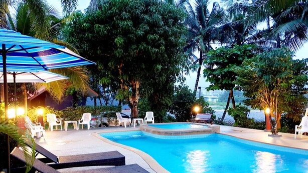 A swimming pool with lounge chairs and umbrellas, surrounded by trees and a view of the ocean. - Mild Garden View Resort (Krabi)