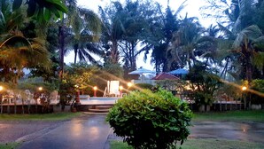 A pathway leading to a seating area with tables and chairs, surrounded by lush greenery and palm trees. - Mild Garden View Resort (Krabi)
