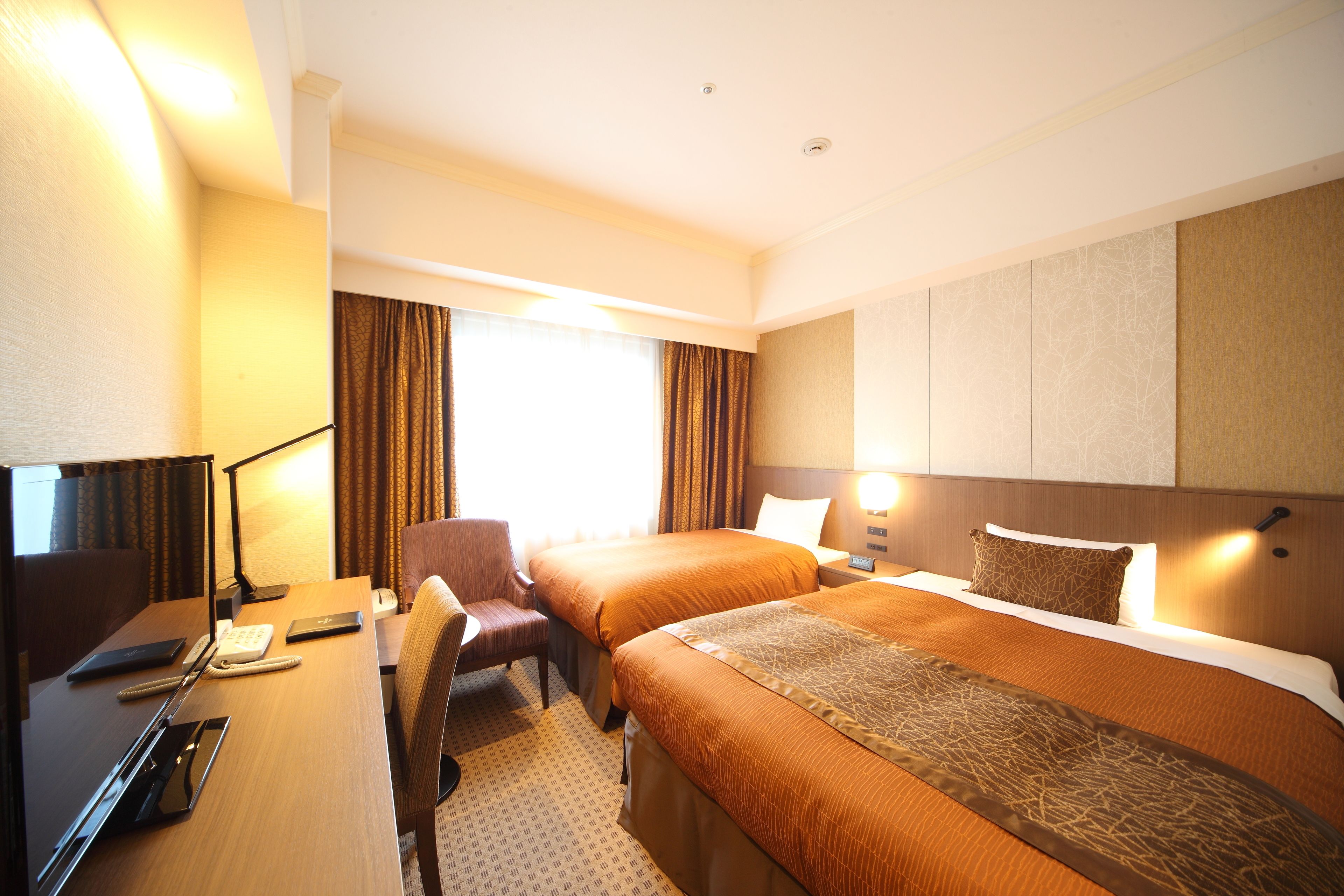 A hotel room with two beds, a desk with a computer, a chair, and a lamp.