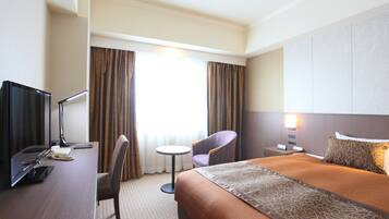 Habitación de hotel con cama, escritorio con computadora, silla, mesita y mesita de noche con lámpara.
