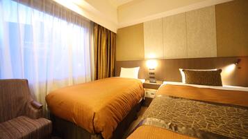 Habitación de hotel con dos camas, una silla, una mesita de noche y una lámpara.