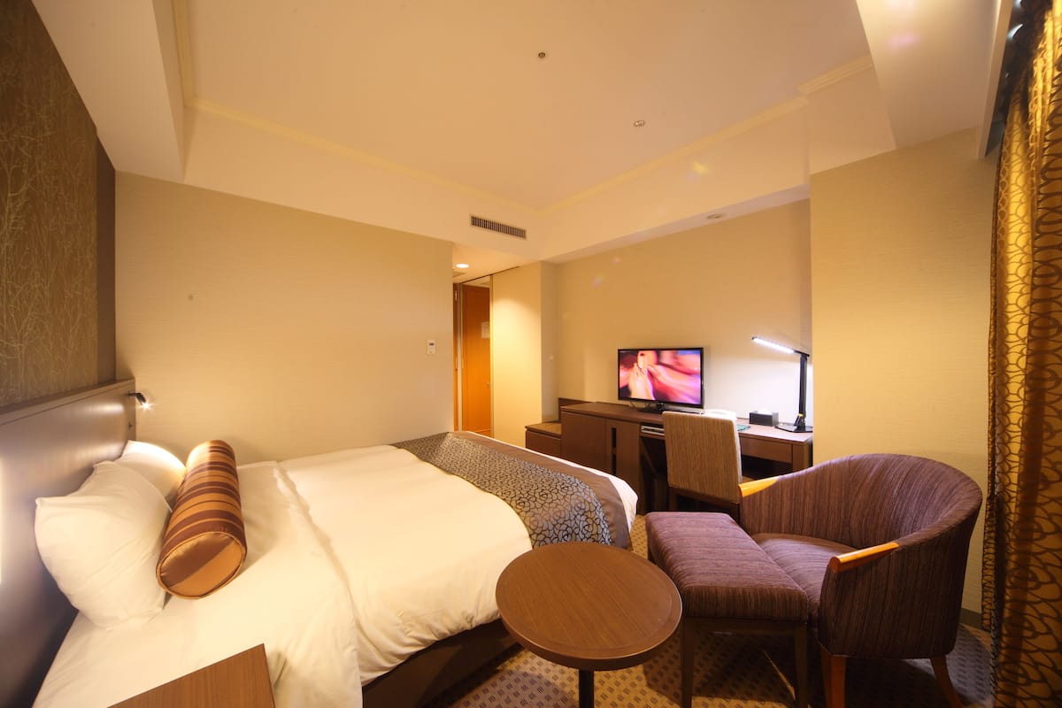 A hotel room with a bed, a desk, a chair, and a television.