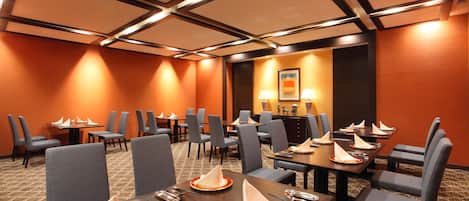A conference room with tables set for a meeting, equipped with chairs and a projector screen.
