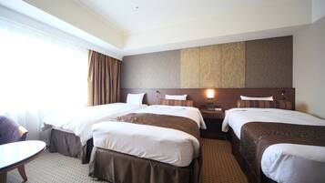 A hotel room with three beds, a desk, and a window with curtains.