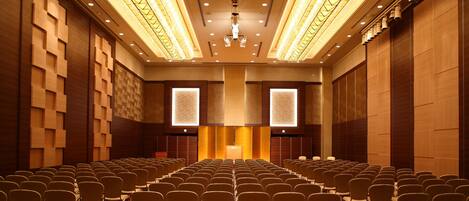 A conference room with rows of chairs, a podium, and a large screen at the front.