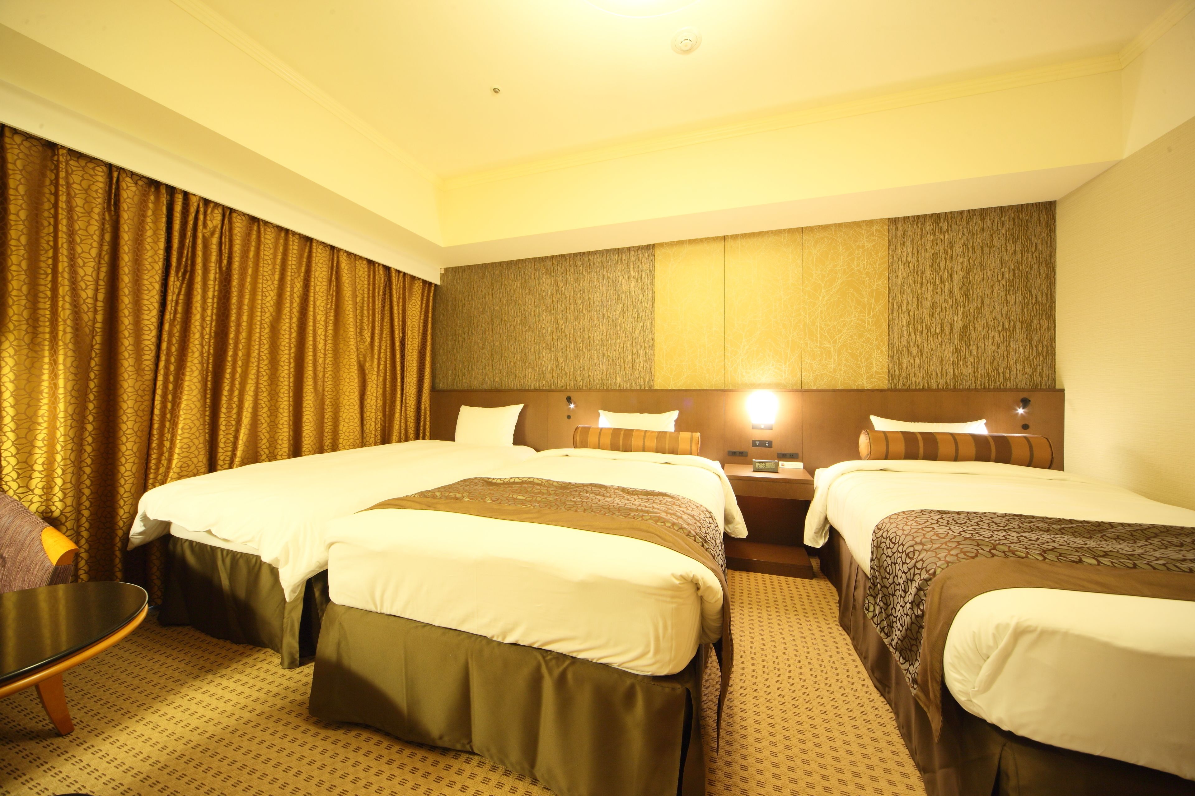 A hotel room with three beds, a small table, and a chair.