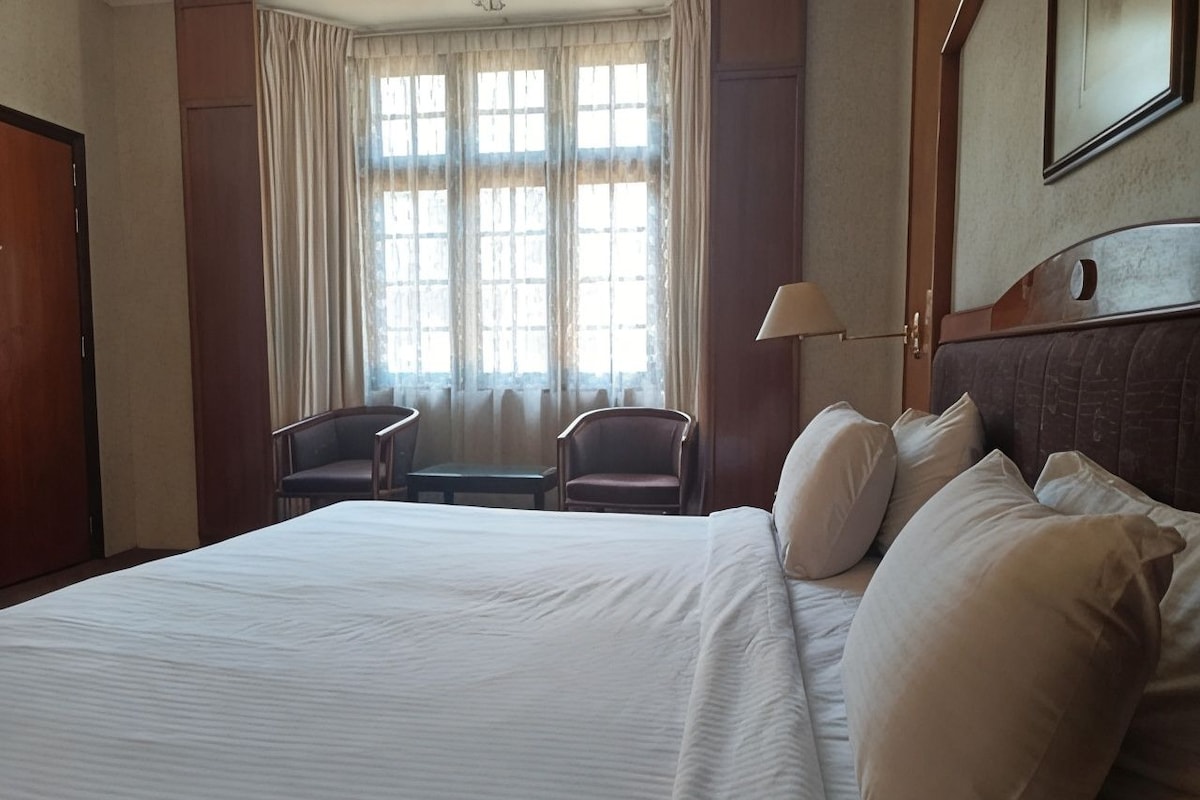 A hotel room with a large bed, two armchairs, a desk, and a window with curtains.