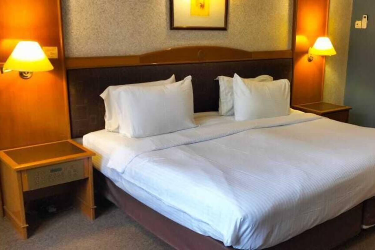 Une chambre d’hôtel avec un grand lit, deux tables de chevet et des lampes fixées au mur.