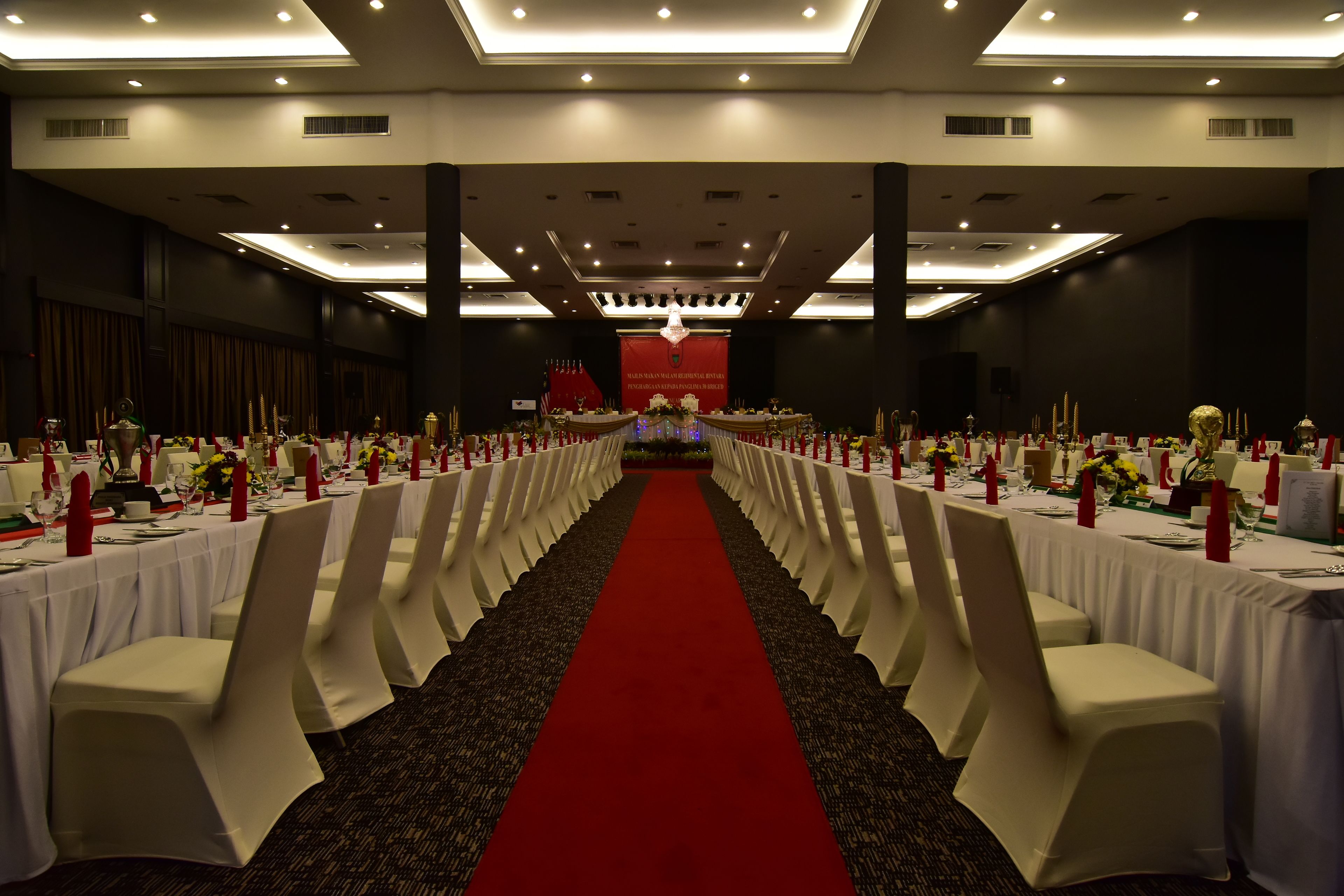 A banquet hall with rows of tables, red carpet, and white chairs.
