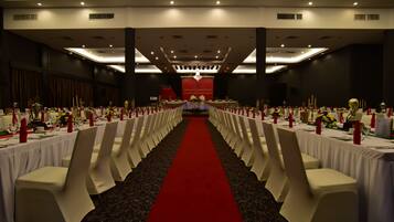 A banquet hall with rows of tables, red carpet, and white chairs.