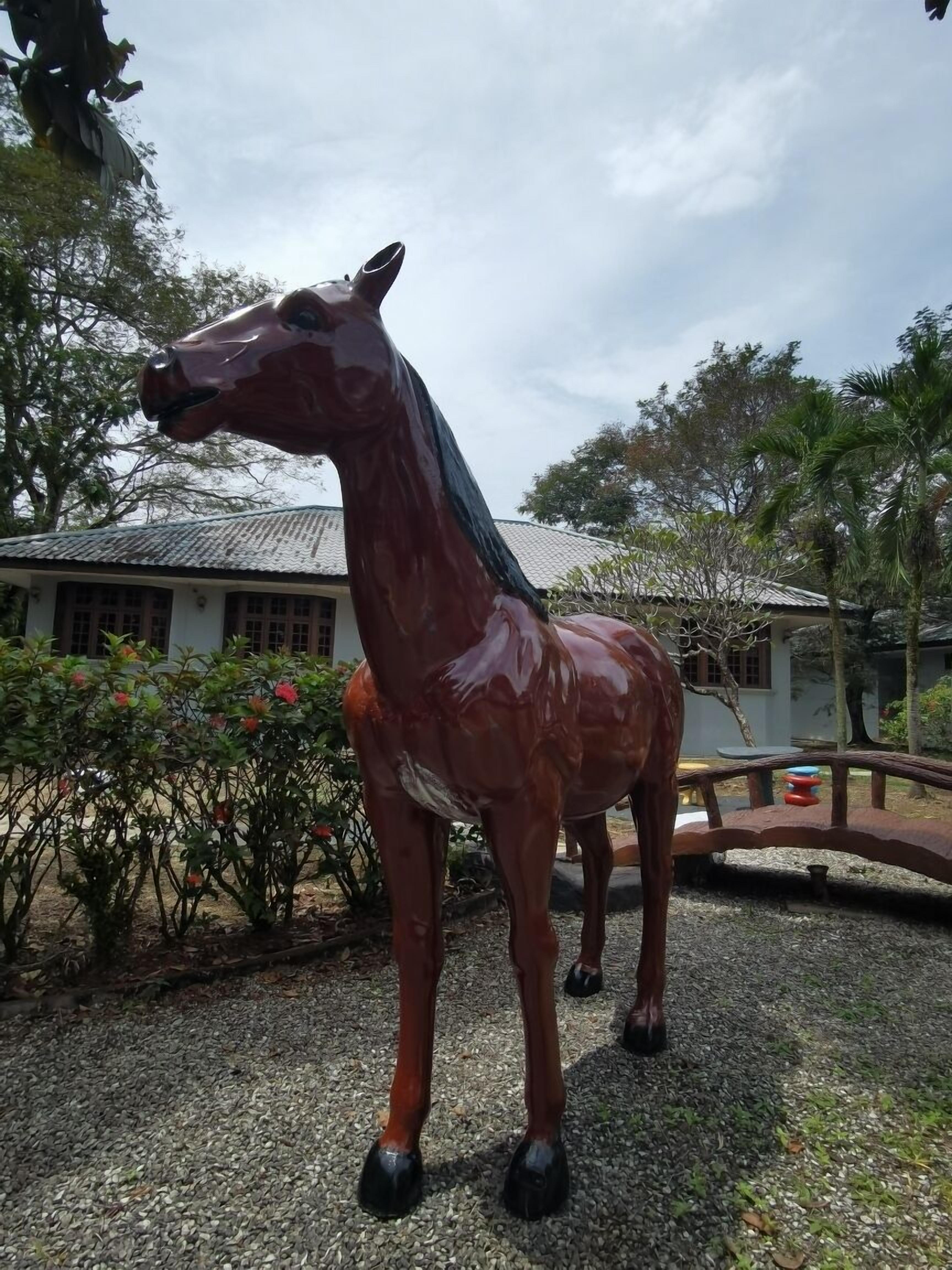 A large, glossy horse statue in an outdoor setting with a building and trees in the background.