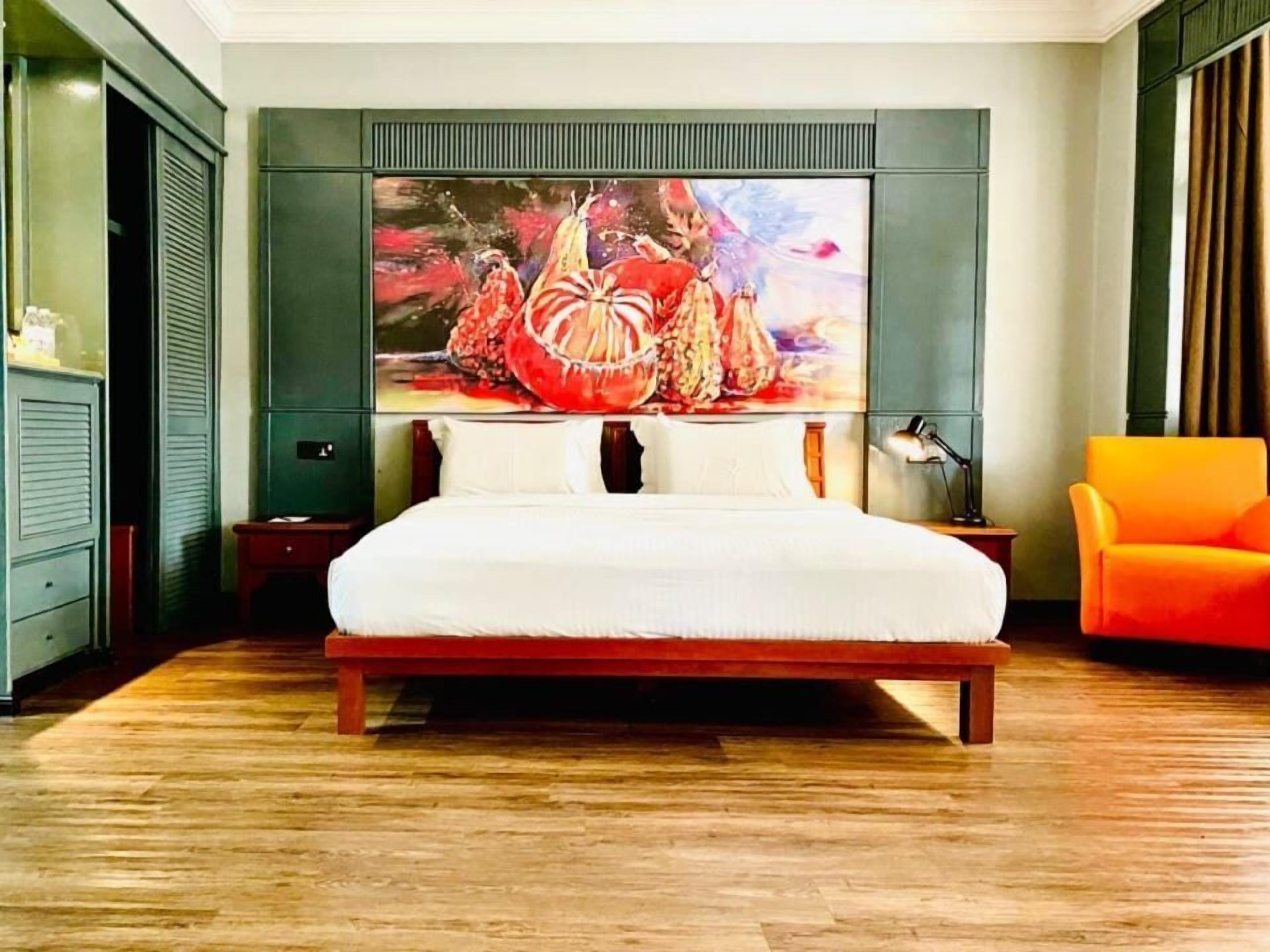 Une chambre d’hôtel avec un grand lit, un tableau au mur, un bureau et une chaise orange.