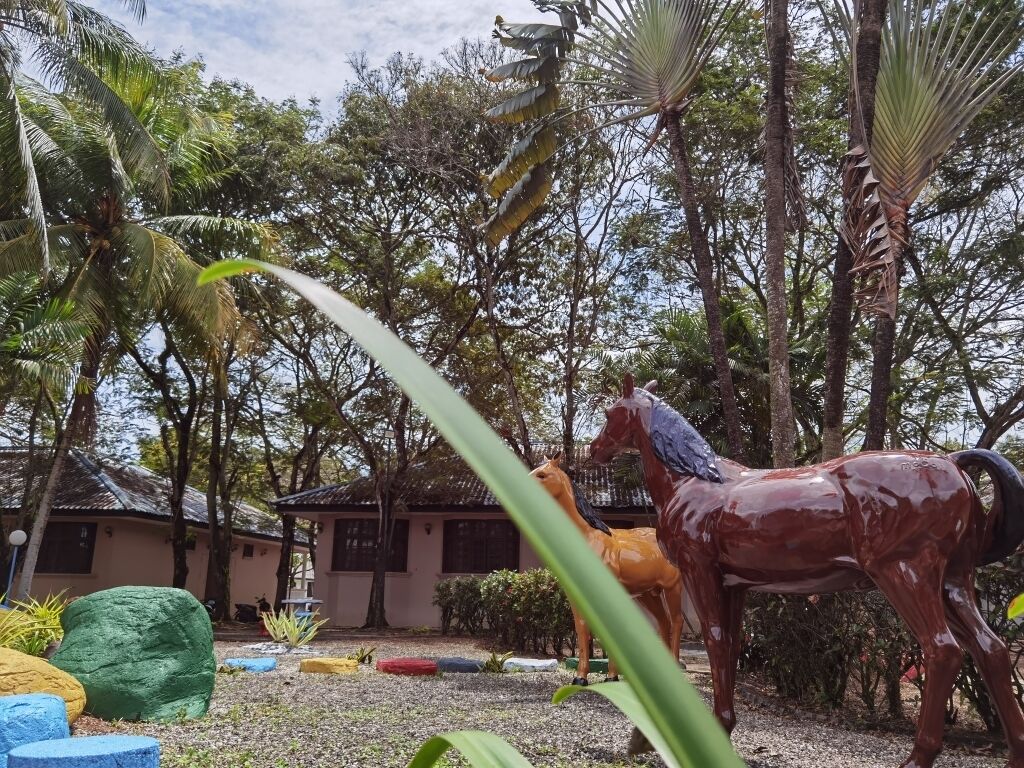 A courtyard with a horse statue, palm trees, and a building in the background.