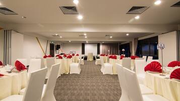 A banquet hall with rows of white chairs and tables, each with red tablecloths and centerpieces.