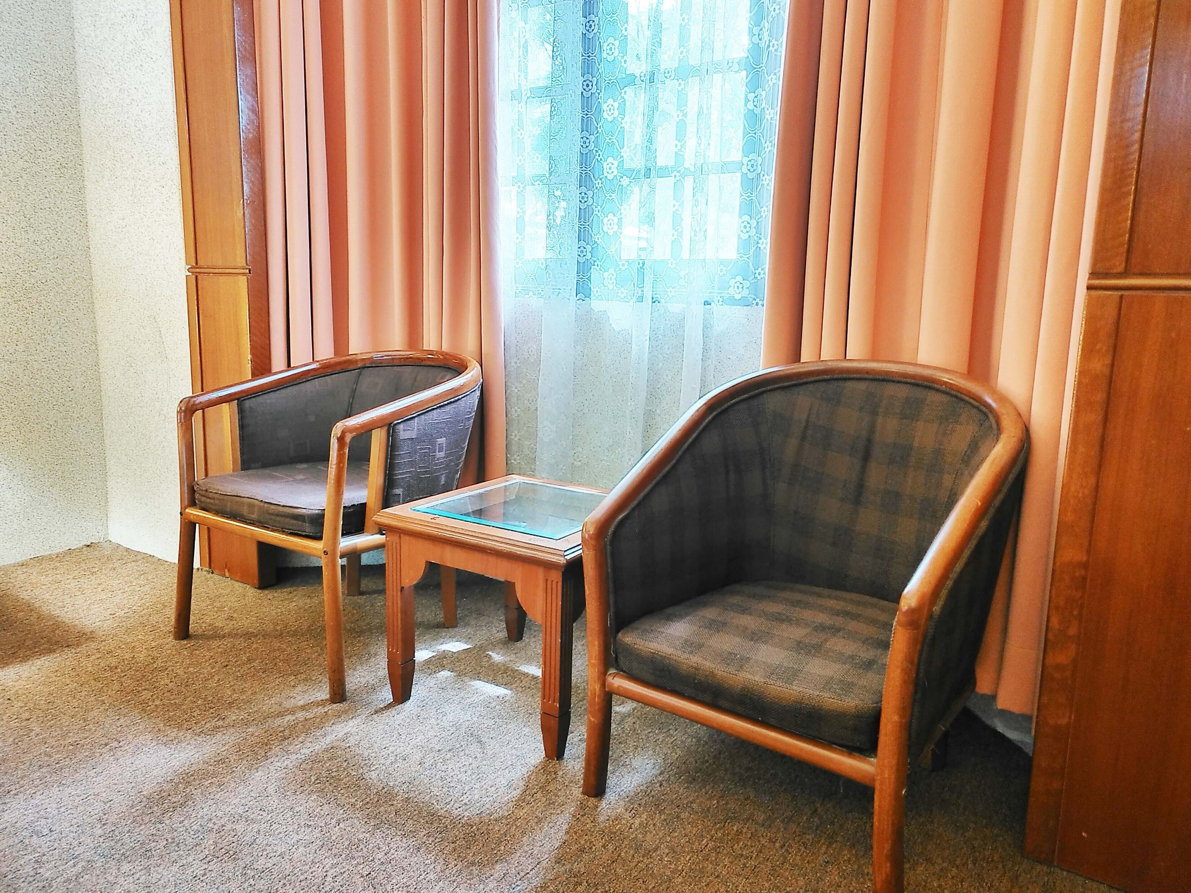 A room with two wooden chairs, a small glass table, and a window with curtains.