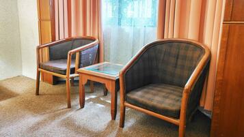 A room with two wooden chairs, a small glass table, and a window with curtains.