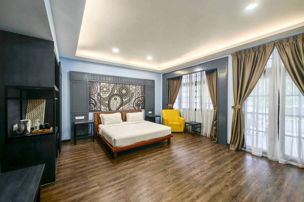 Une chambre d’hôtel moderne avec un plancher en bois, un grand lit, un fauteuil jaune, une petite table et un panneau décoratif mural.