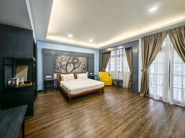 Una habitación de hotel moderna con piso de madera, una cama grande, un sillón amarillo, una mesita y un panel decorativo en la pared.