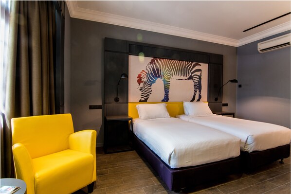 Habitación de hotel con una cama, un sillón amarillo, una mesita de noche y un mural con motivos de cebra en la pared.