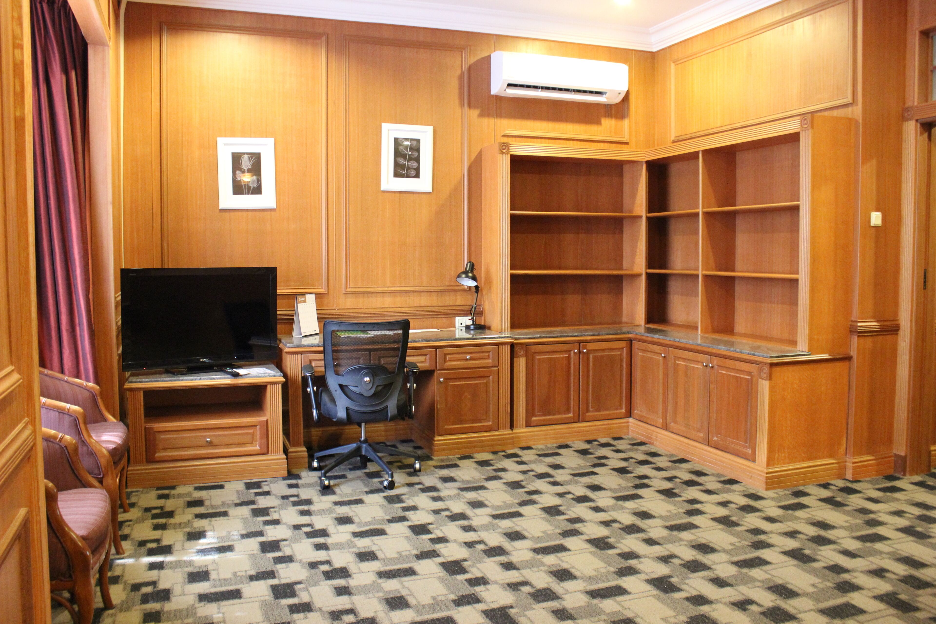 A room with wooden paneling, a flat-screen TV, a desk with a chair, and a patterned carpet.