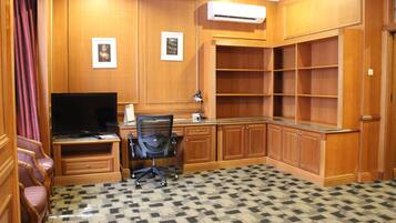 A room with wooden paneling, a flat-screen TV, a desk with a chair, and a patterned carpet.