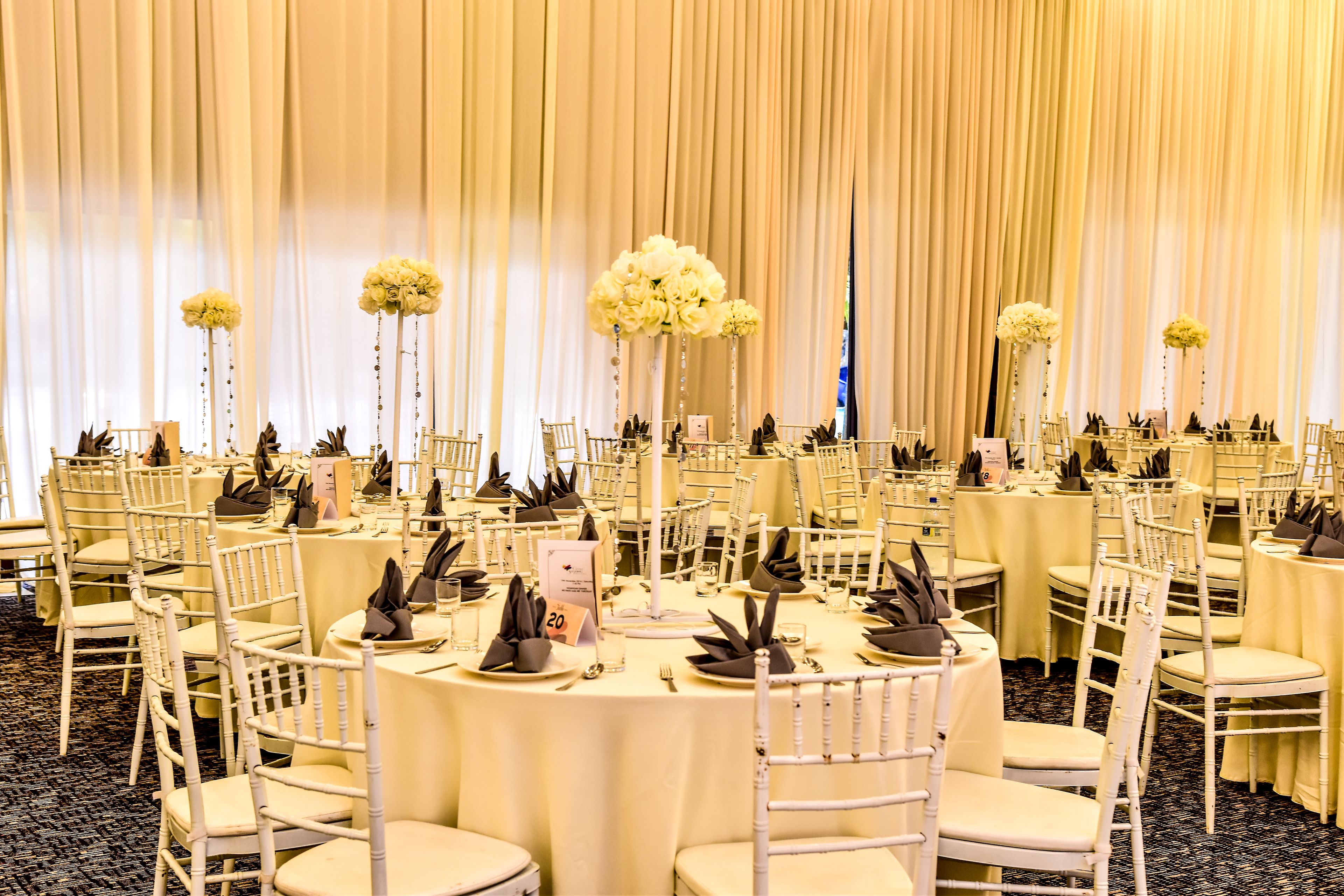 Un salón de banquetes con mesas redondas, sillas blancas y centros de mesa florales.