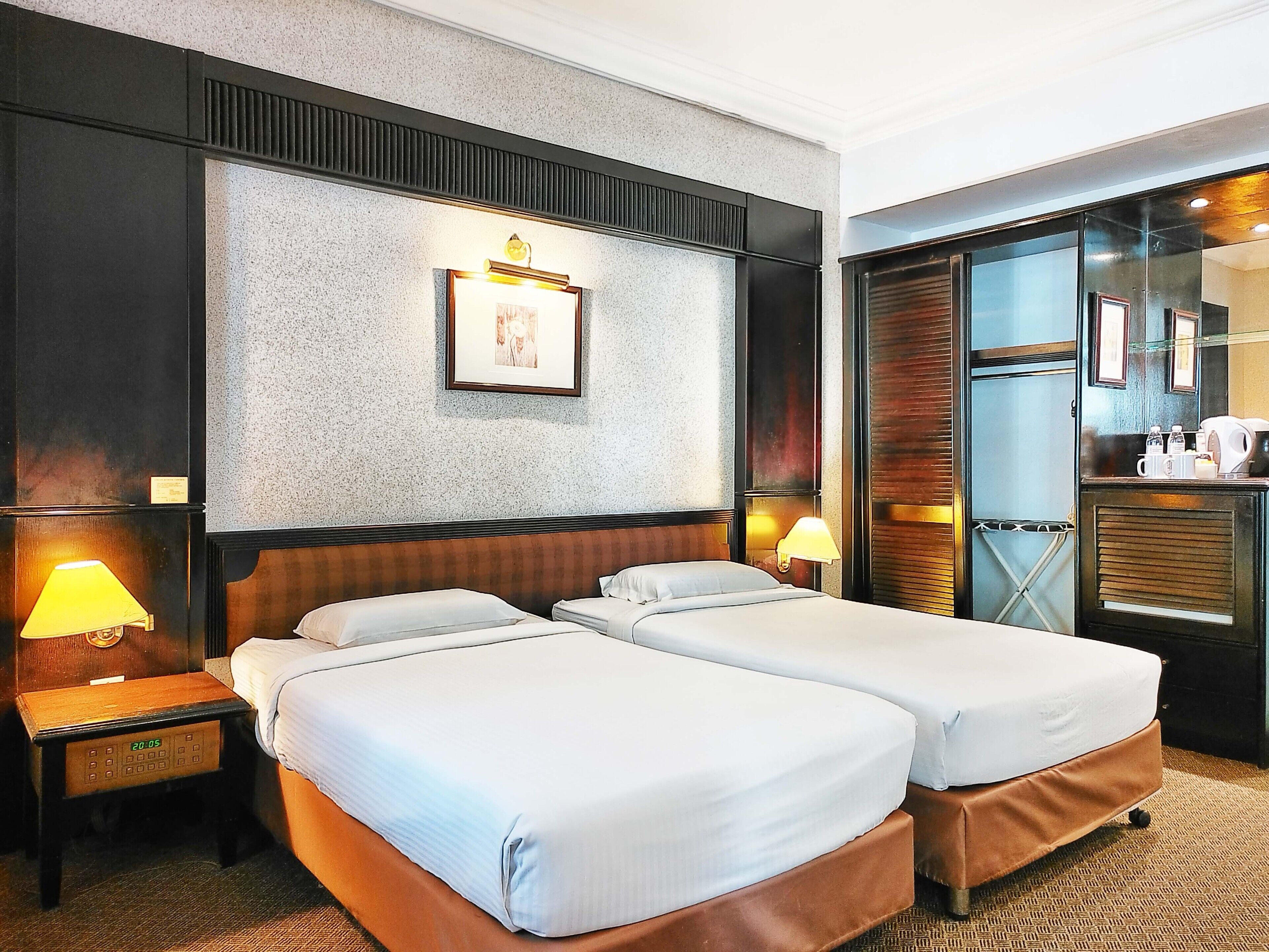 A hotel room with two beds, a nightstand, a lamp, a framed picture on the wall, and a minibar.